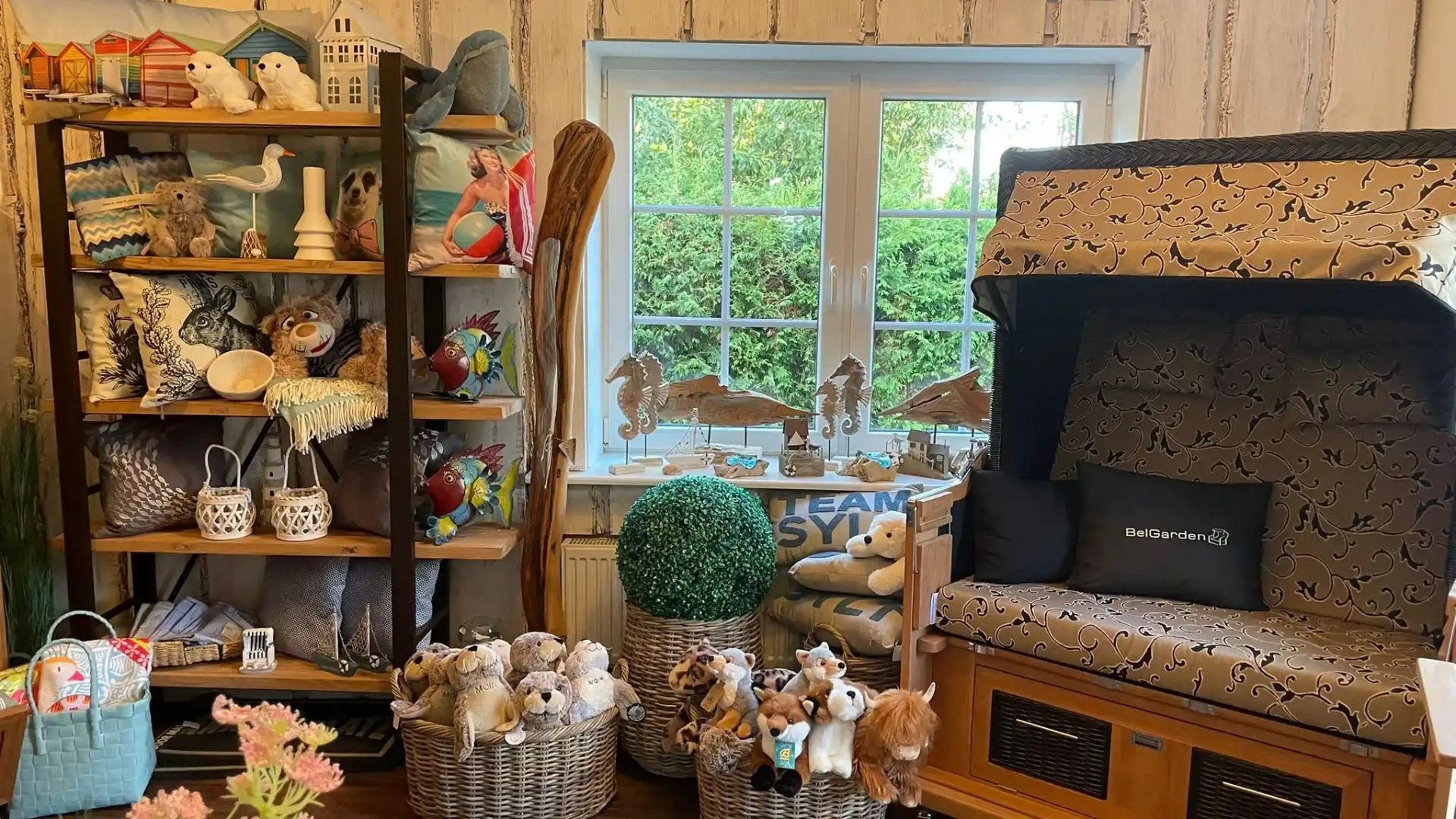 BelGarden Strandkorb mit dunklem Polster neben Deko-Regal und Holz-Seepferdchen am Fenster